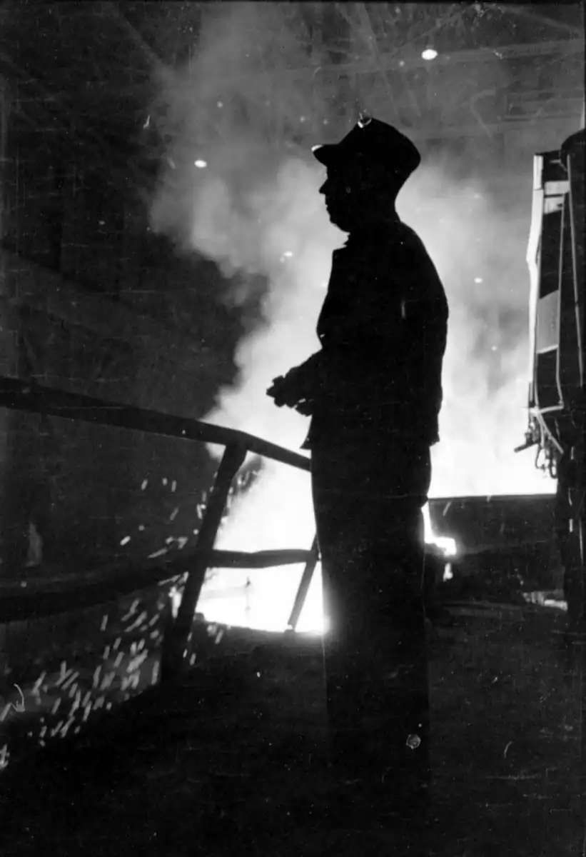 A steelworker silhouetted against molten metal, 1949